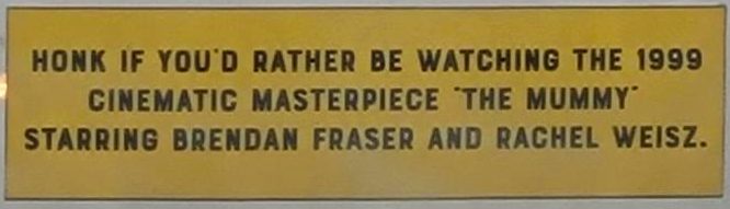 yellow bumpersticker, with the text: HONK IF YOU'D RATHER BE WATCHING THE 1999 CINEMATIC MASTERPIECE THE MUMMY STARRING BRENDAN FRASER AND RACHEL WEISZ.